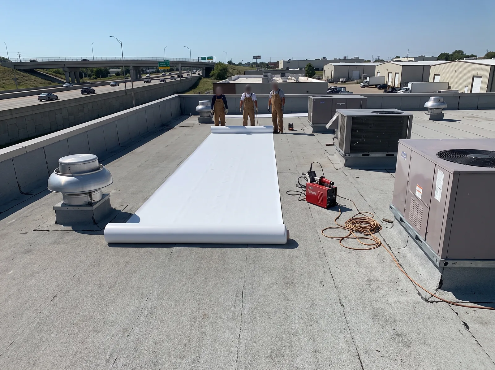 White TPO membrane being rolled out on a low-slope commercial roof with a Tulsa-area industrial park beyond